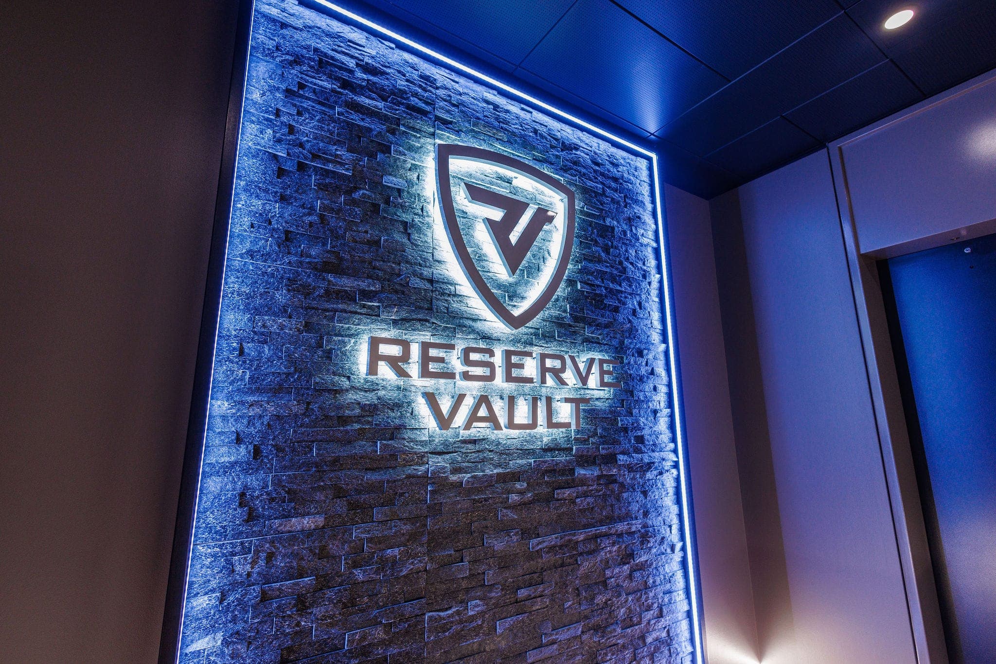The illuminated Reserve Vault shield and wordmark on a backlit stone wall