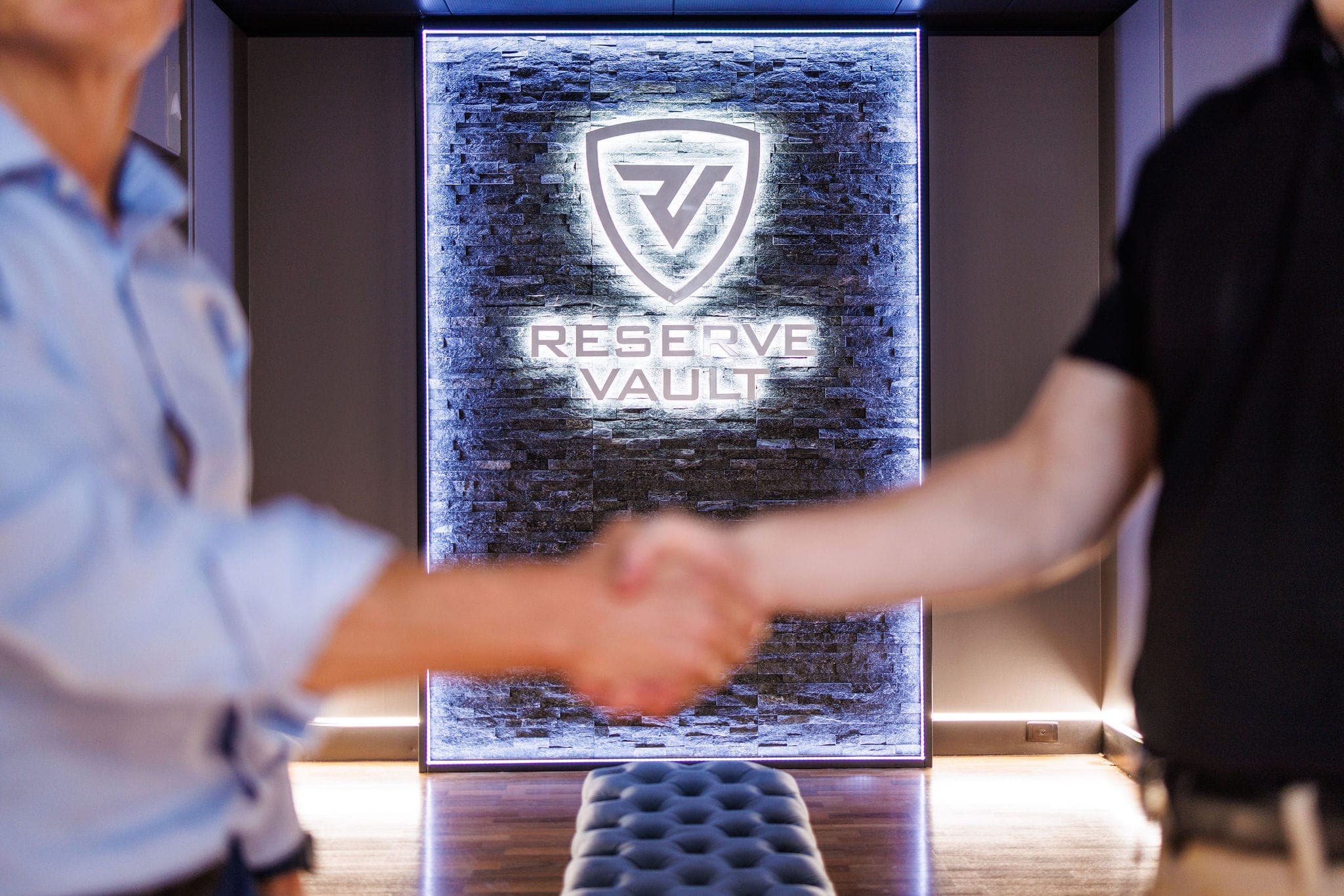 A handshake in front of the illuminated Reserve Vault logo wall in the lobby